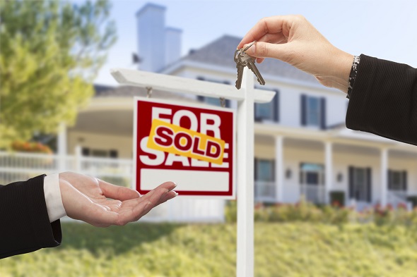 Agent Handing Over Keys to a New Home with Sold Real Estate Sign and House in the Background.